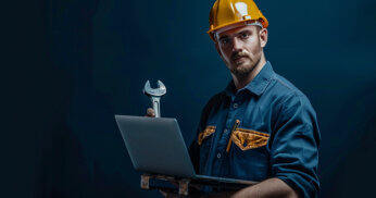 Man wearing hard hat carrying a laptop, holding wrench in hand.