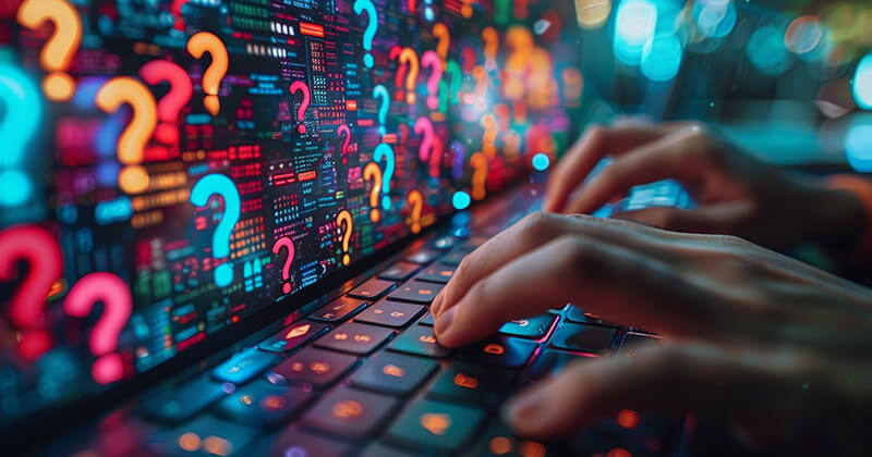 Fingers typing on keyboard; colorful question marks displayed on computer screen.